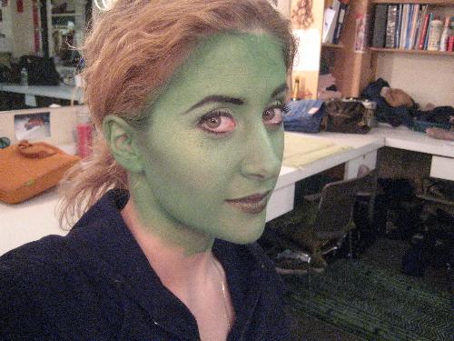 a person with a green face painted in the middle of a room