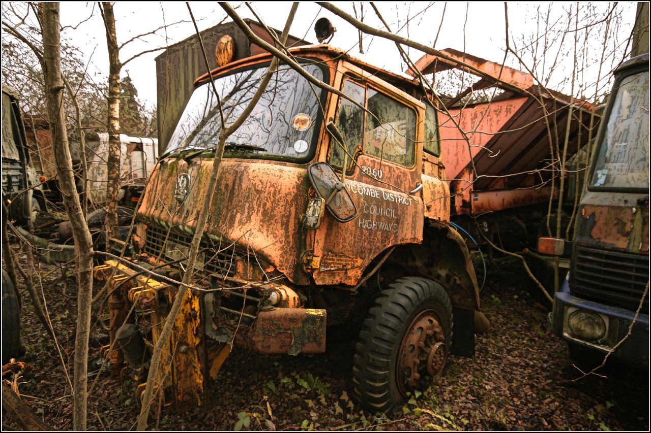 an old truck in a junkyard surrounded by trees