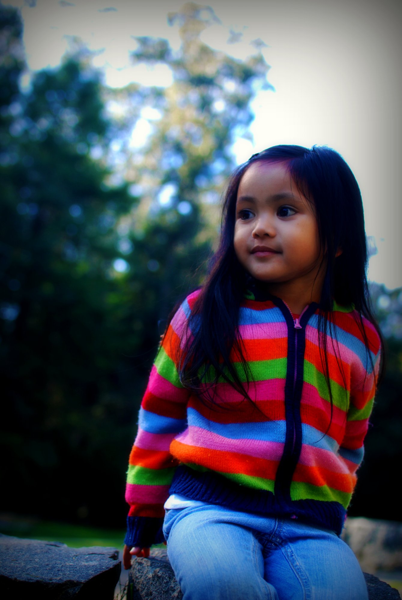 a little girl is sitting on a rock