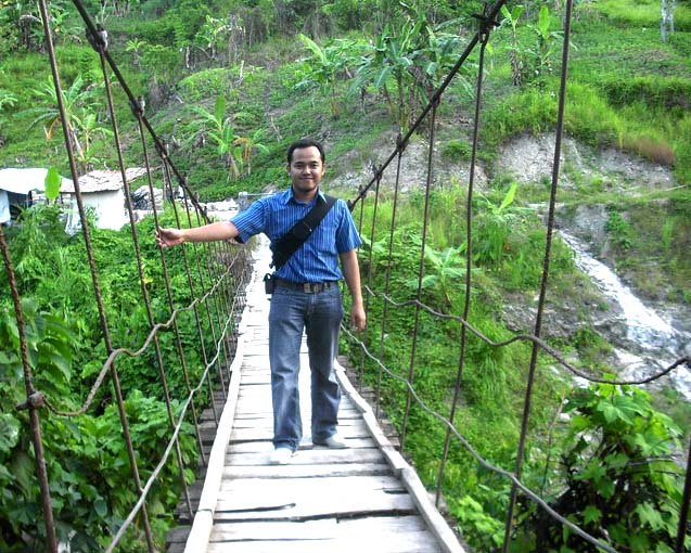 man in a blue shirt crossing a rope bridge over water