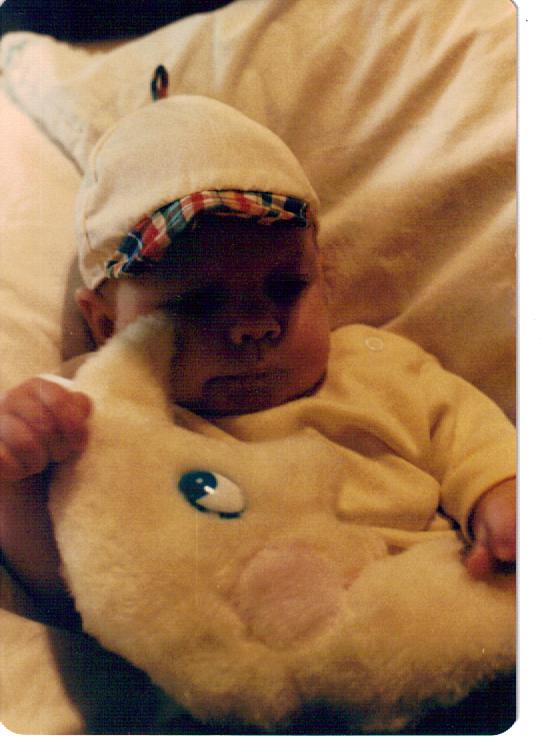 a toddler dressed in a yellow outfit, laying down with a teddy bear