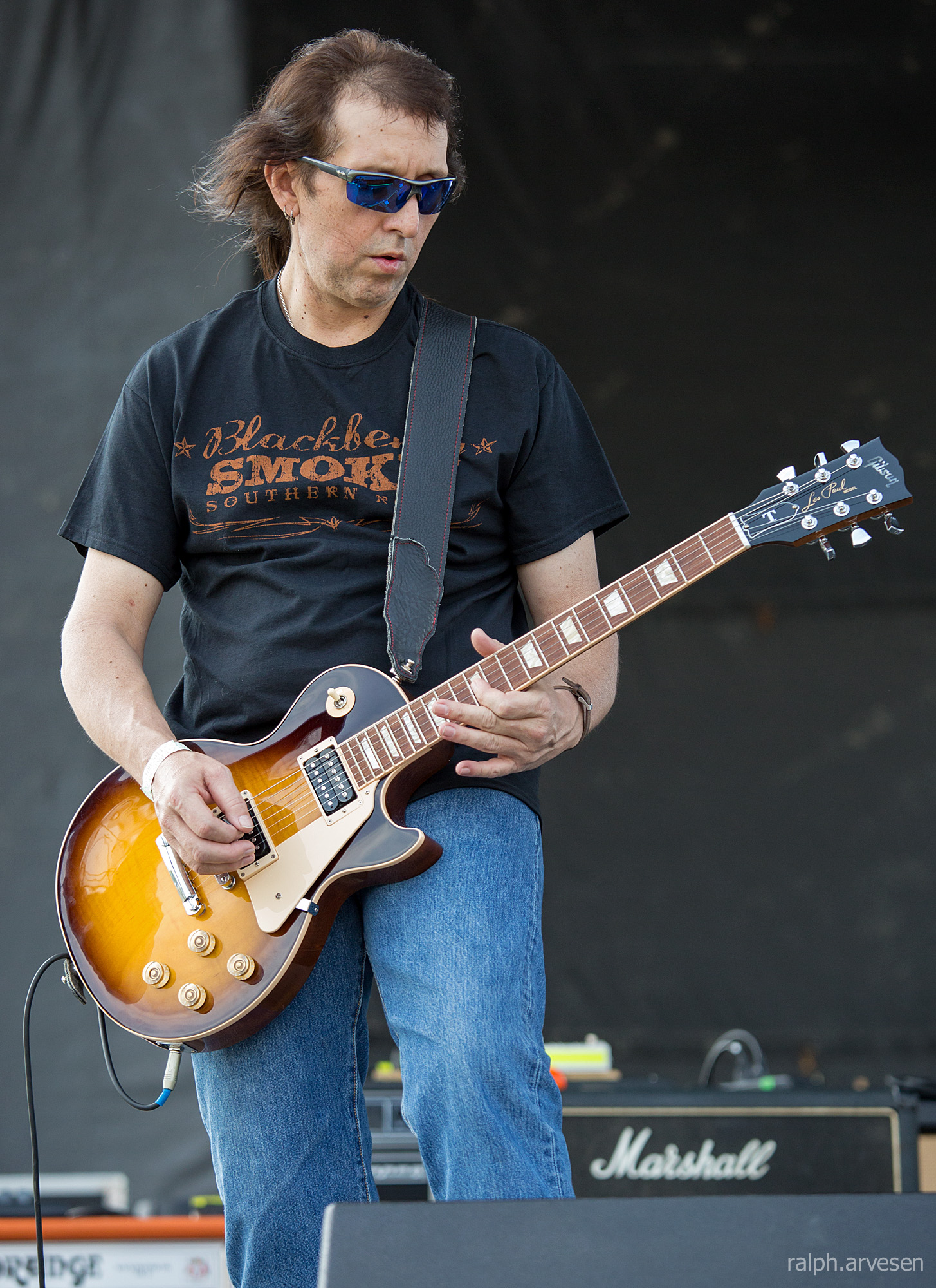 a man with sunglasses plays an electric guitar at an outdoor concert