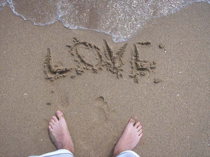someone is writing love in the sand at the beach