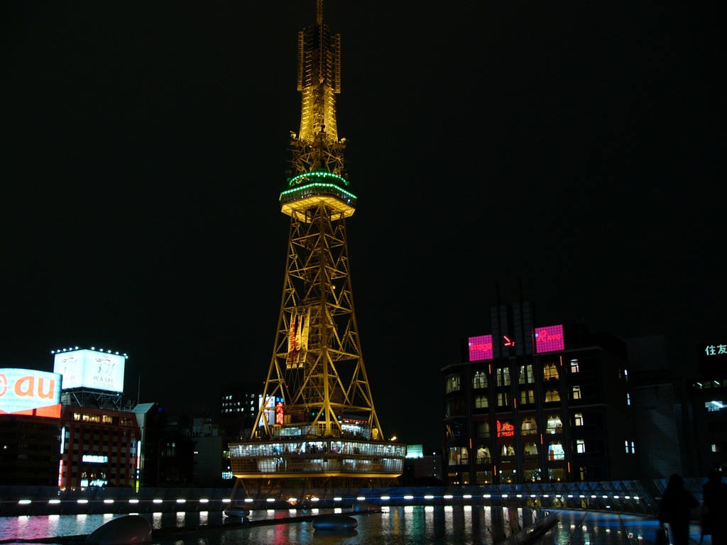 the lit up television tower is reflecting in the water