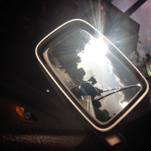 the rear view mirror of a car shows the sun shining through the trees