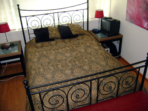 an ornate metal bed with wooden floors and a red chair