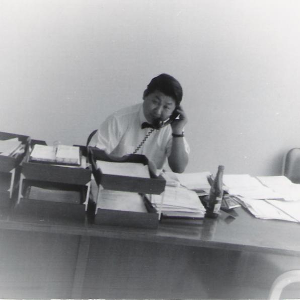black and white pograph of an older man at a desk while talking on the phone