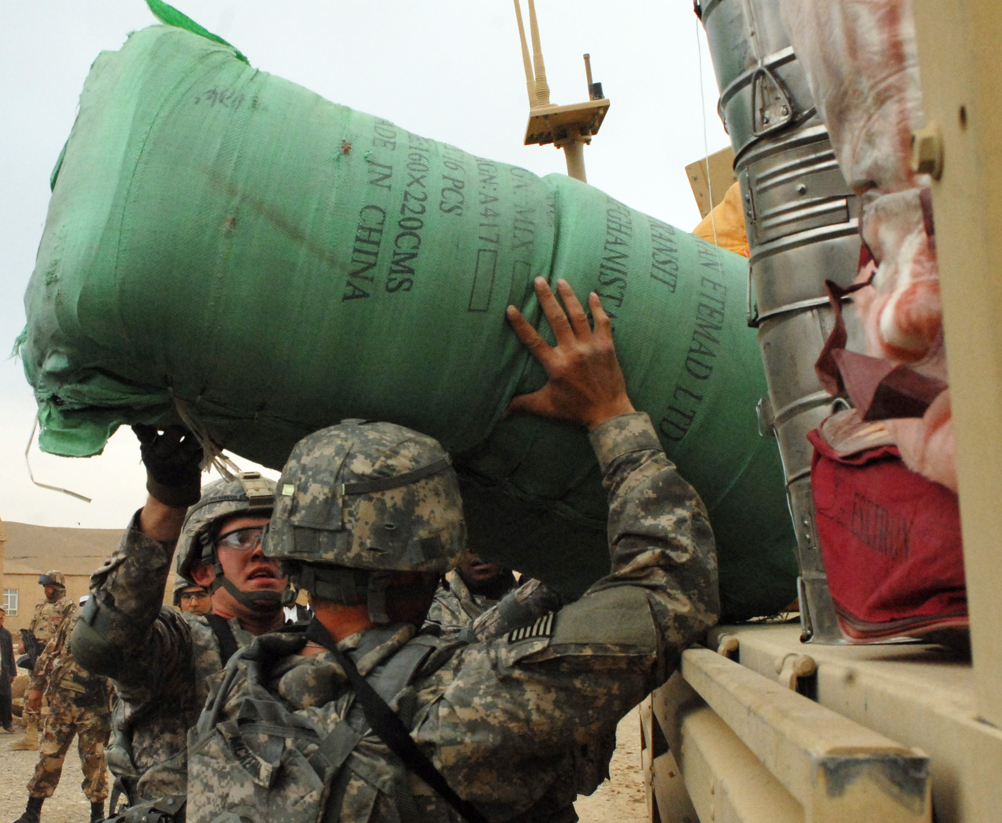 soldiers carry bags of cargo onto the back of a truck