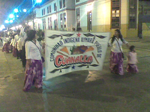 a group of women and  in purple skirts carry a banner that reads, gumerbee