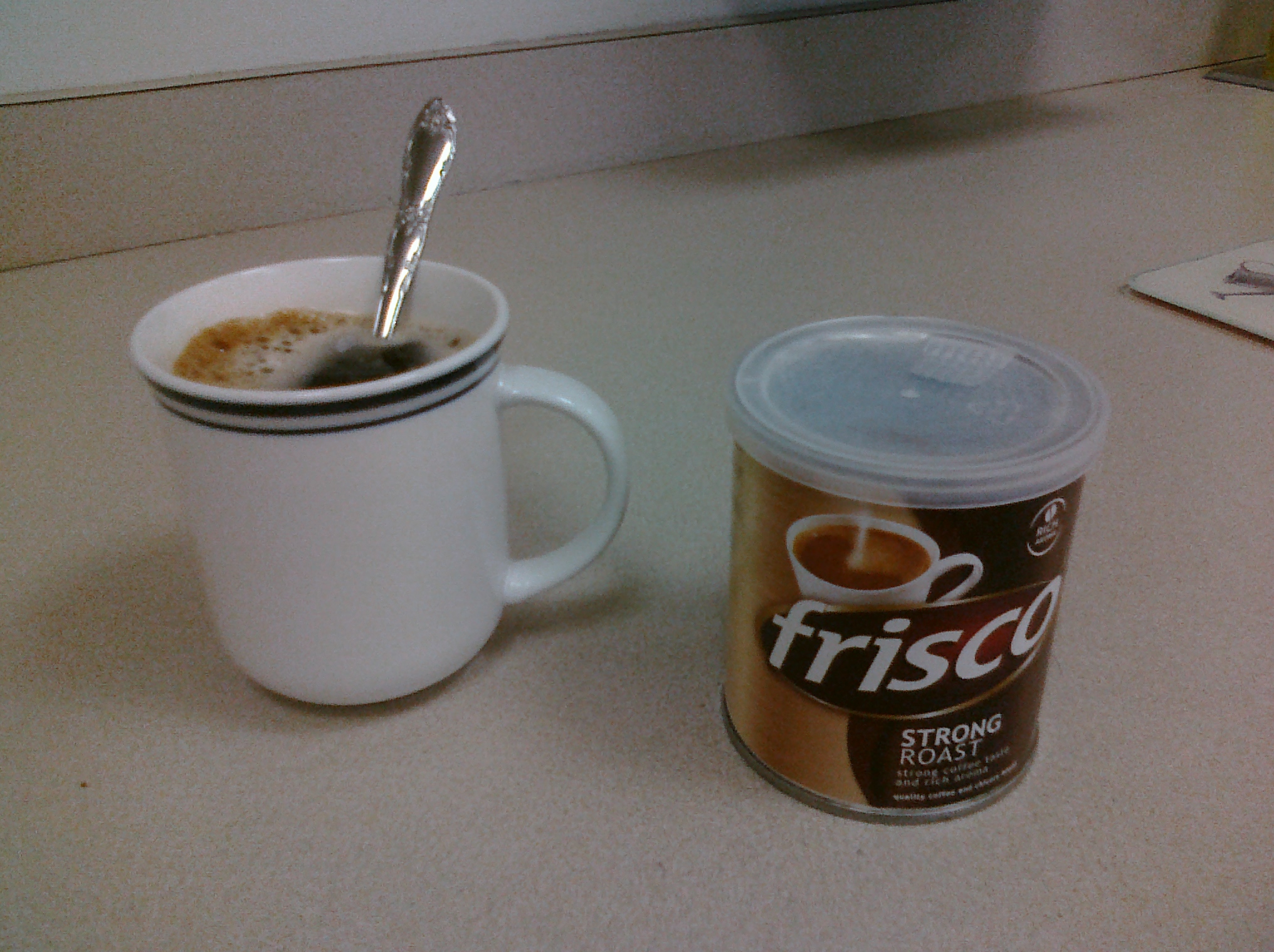 a coffee cup with a spoon is next to a can of frisca
