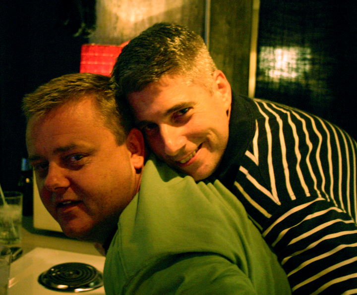 two men smiling next to each other at a restaurant