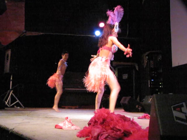 two women perform on a stage with one wearing a feathered dress