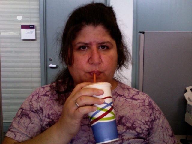 a woman drinking a cold drink while sitting in an office