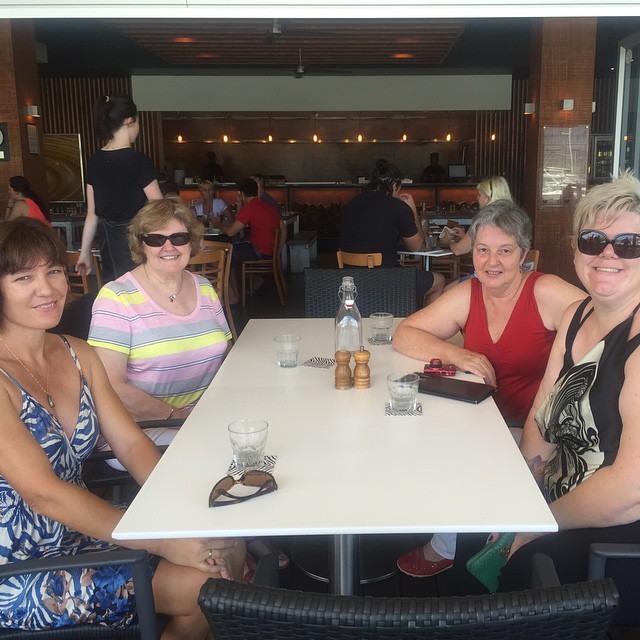 four women sitting at a restaurant table wearing sunglasses