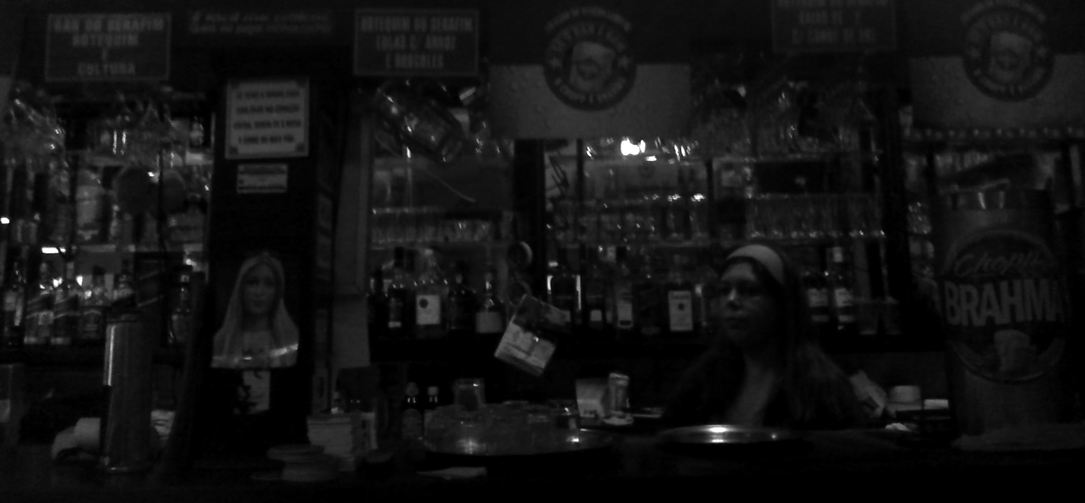 black and white pograph of woman sitting in front of counter with bottles