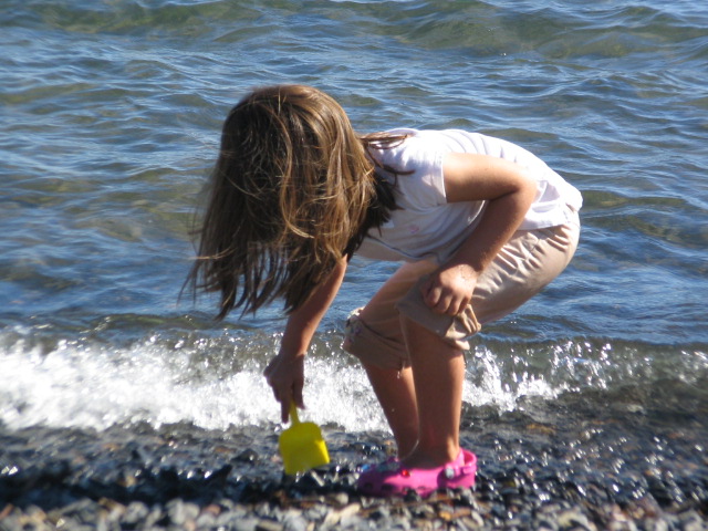 a child is playing in the water on rocks at the edge of the beach
