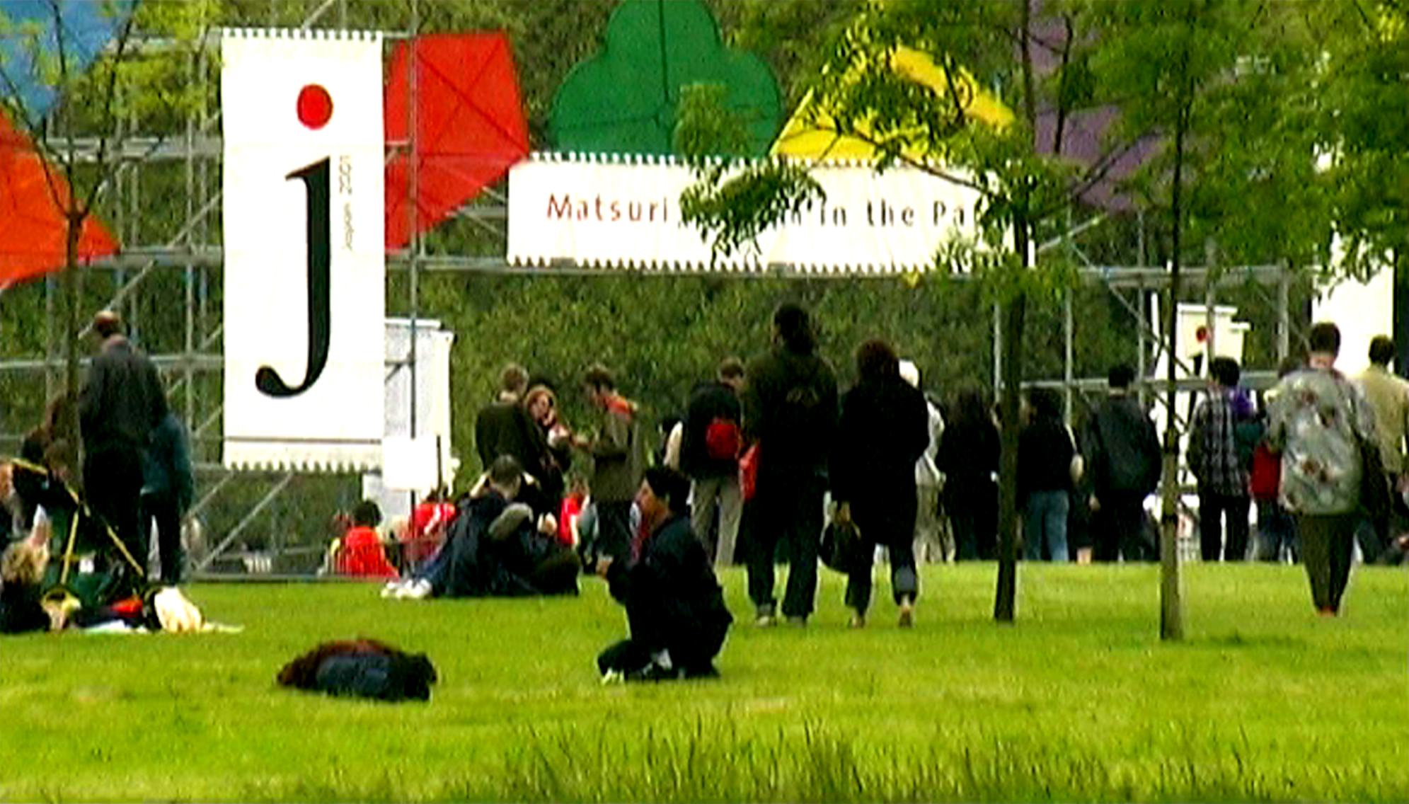 people sit and stand on the grass outside