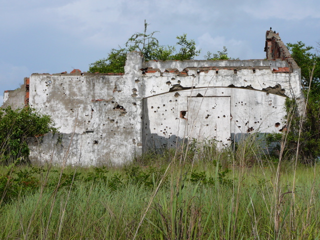 a dilapidated building with bullet holes and trees on top