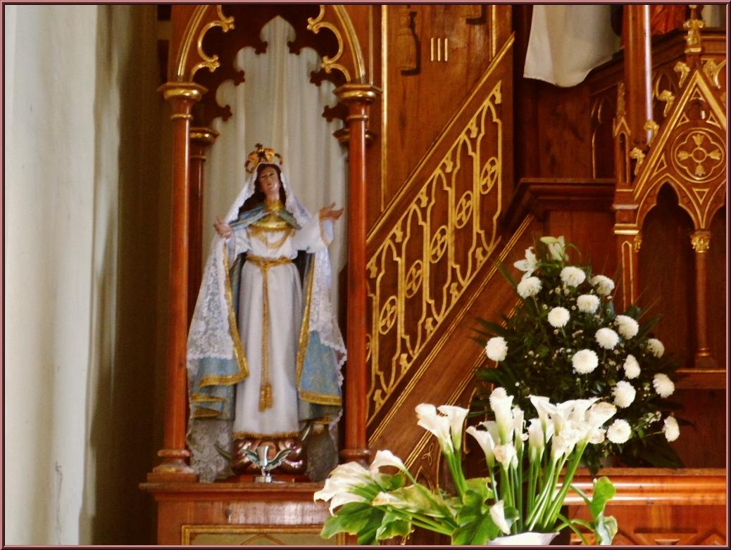 a statue of virgin mary stands before a vase of white flowers and a floral arrangement