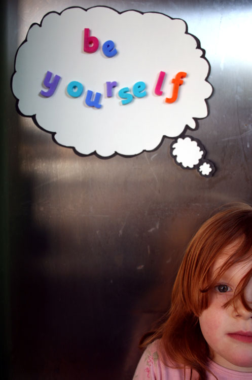 a girl looks into the camera while she stands in front of a metal refrigerator