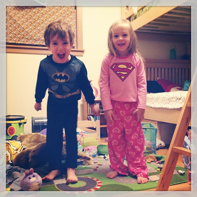two children stand on the floor while dressed up in superman pajamas