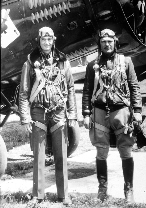 two men in flight gear standing by an airplane