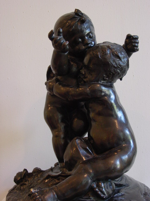 a bronze statue holding an infant sitting on top of a wooden table