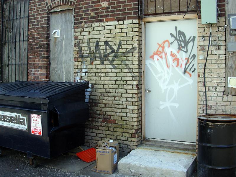 a brick building with spray painted graffiti next to a garbage can