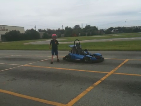 a boy standing in the parking lot near an electric race car