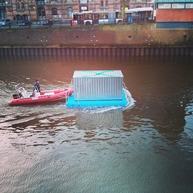 a red boat in the water near a white container