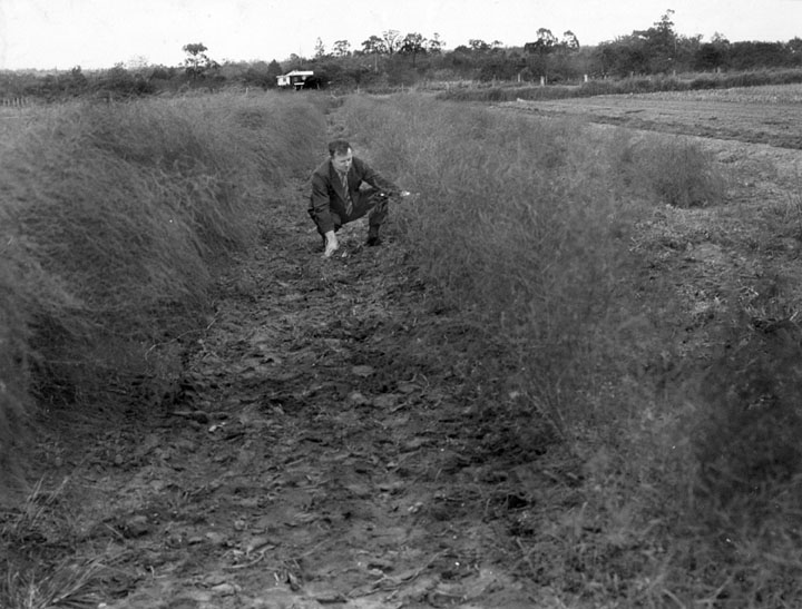 a man kneeling on a dirt path in a field