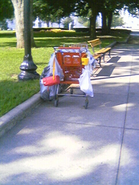 a shopping cart parked on a sidewalk filled with plastic bags