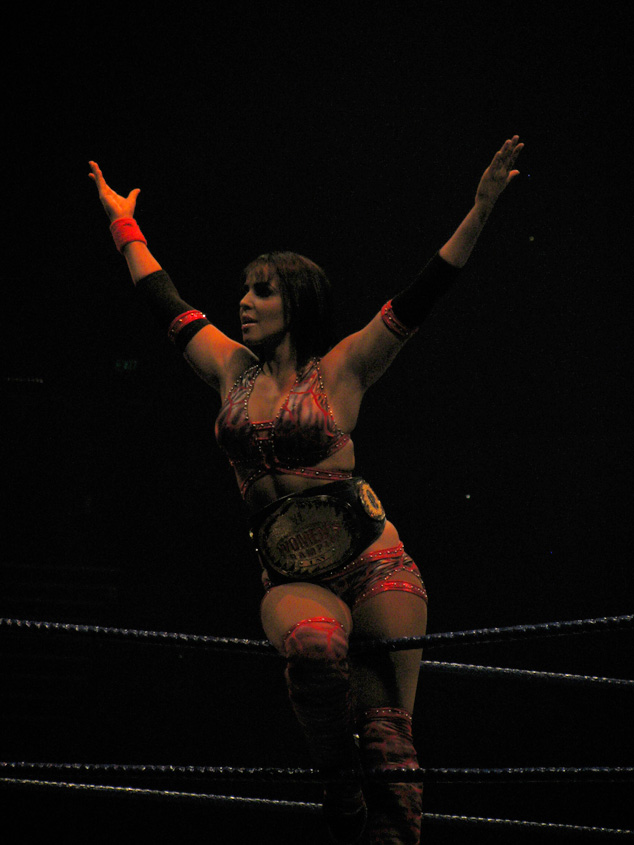 a female wrestler standing in a ring with her arms raised