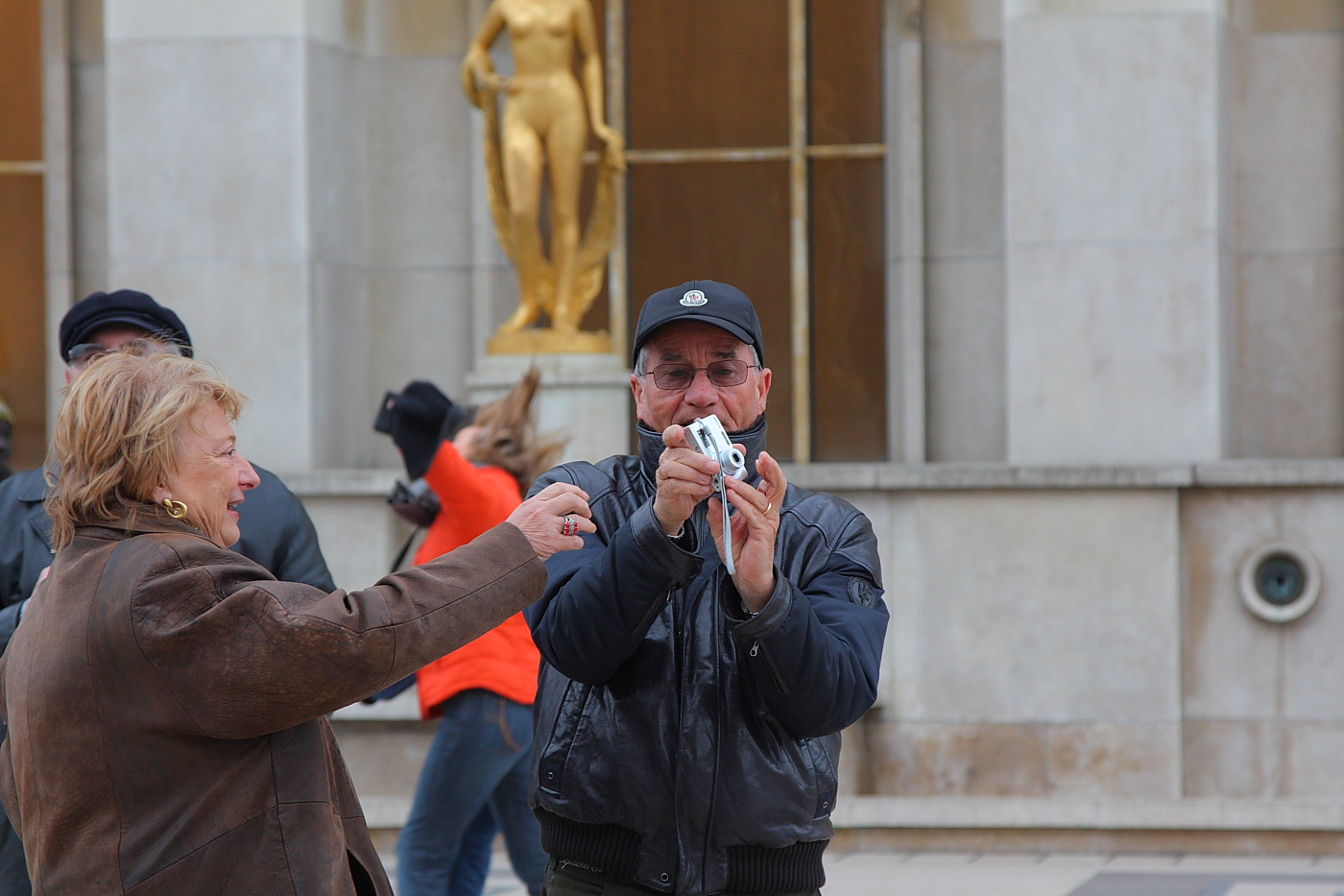 an older woman pographing the camera while a man in hat holds out his phone