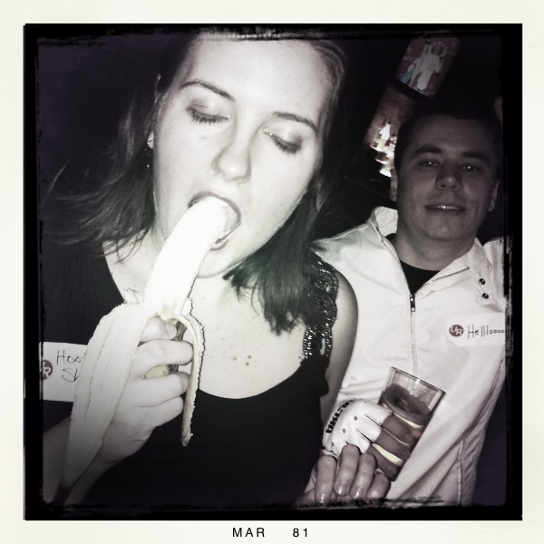 a woman sticking a banana in her mouth next to a man