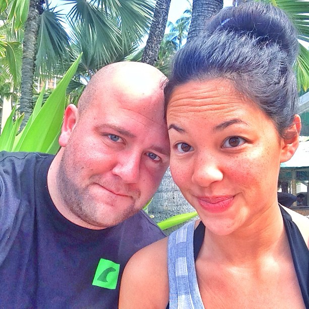 two people pose for the camera in front of palm trees