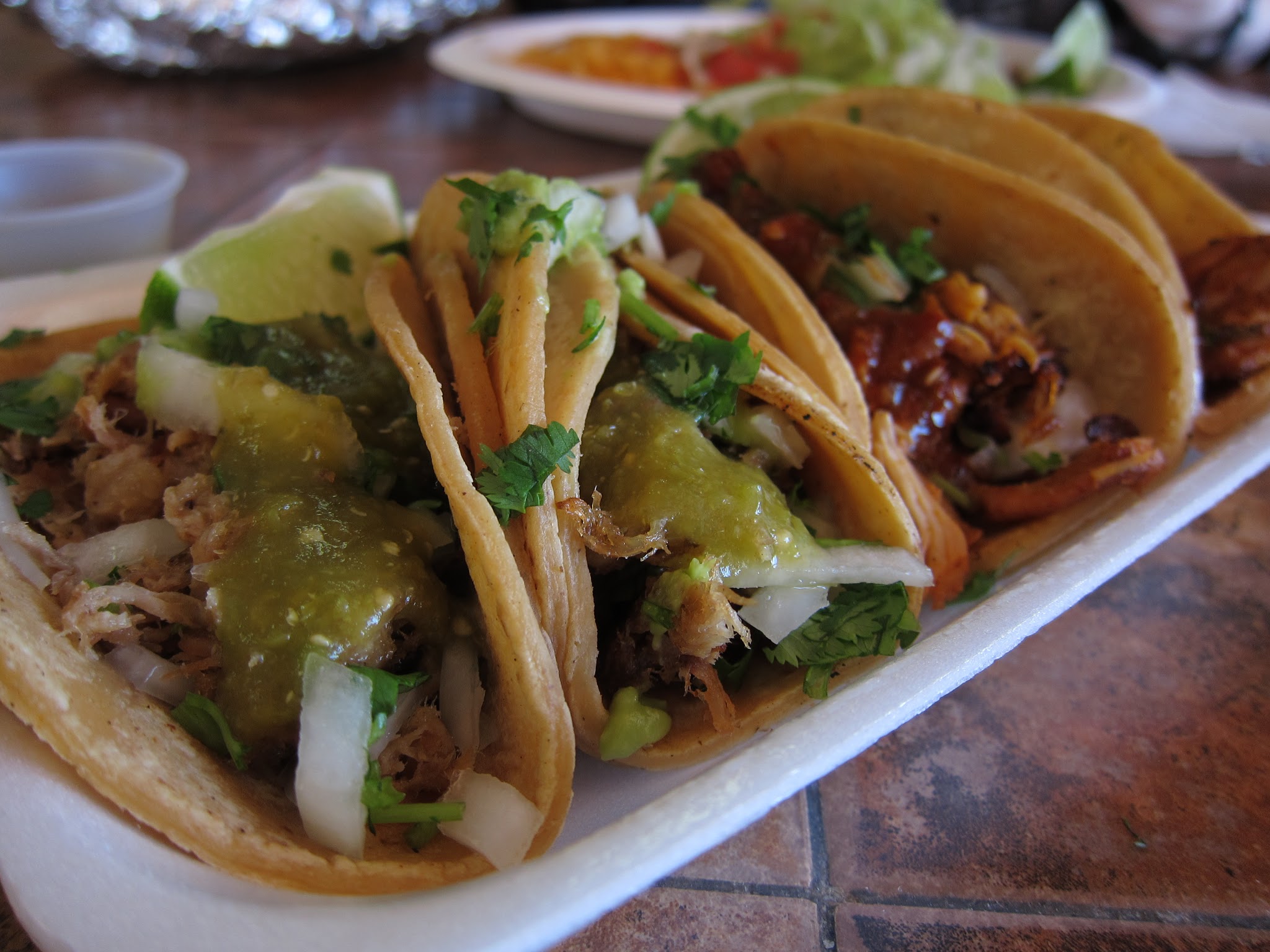 three tacos on a plate next to other food
