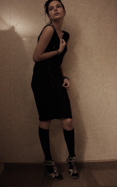 woman standing with legs crossed, dressed in black dress and socks