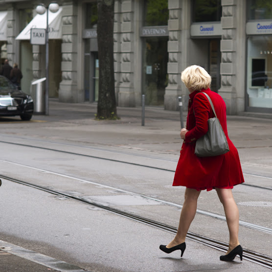 the blonde haired woman in a red dress is crossing the street