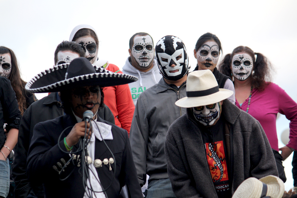 people in costume and mexican masks sing and dance