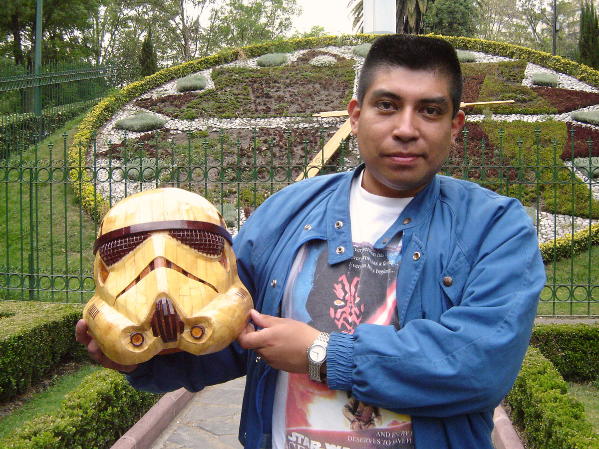 a man holding a wooden helmet and a clock on the wall behind him