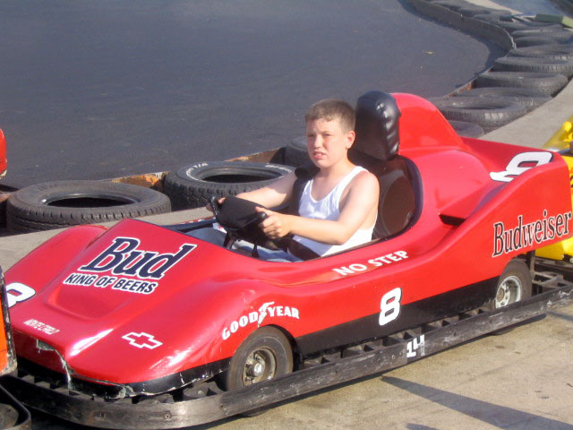 a boy driving a pedal car that is on the ground
