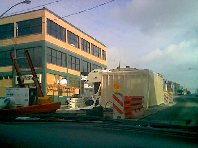 a car driving past a store next to traffic cones and cranes