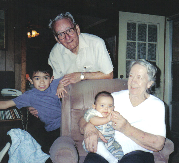 an older man is sitting on a brown chair next to a small child and his father is holding a baby