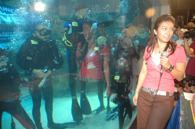 woman in pink shirt standing next to aquarium with various people