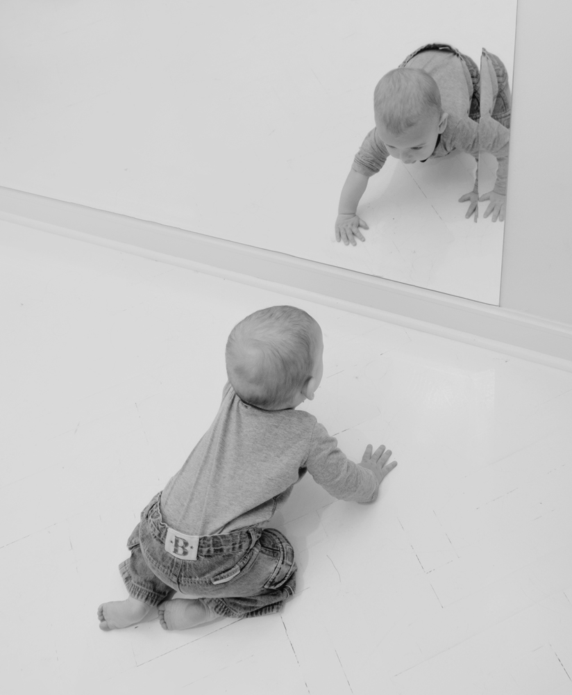 small child sitting on the floor looking at a mirror
