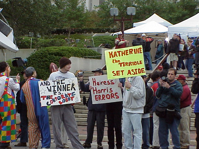 people holding signs standing outside with umbrellas and a white tent behind them