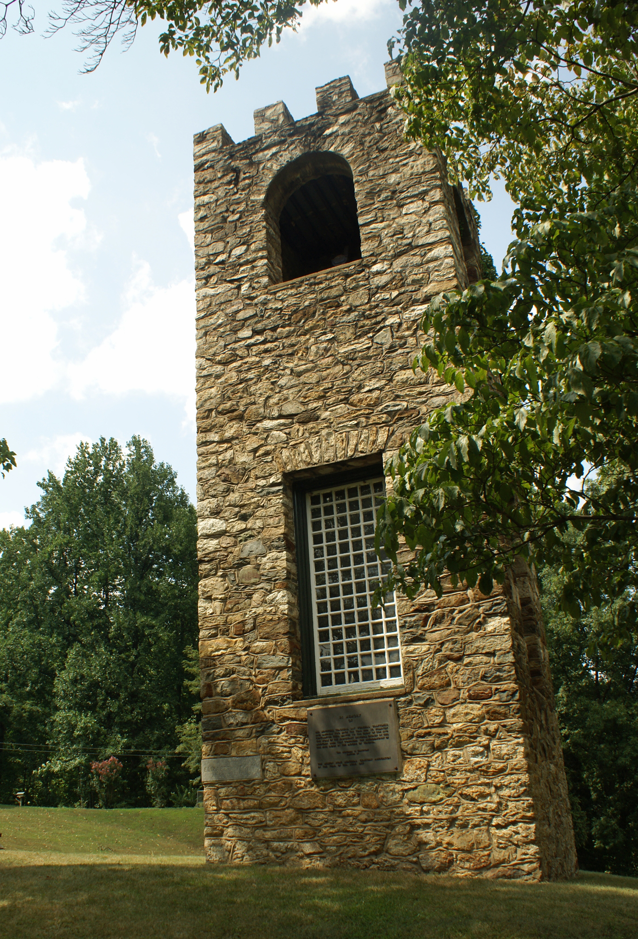 a clock tower with a window inside sits in the middle of a park