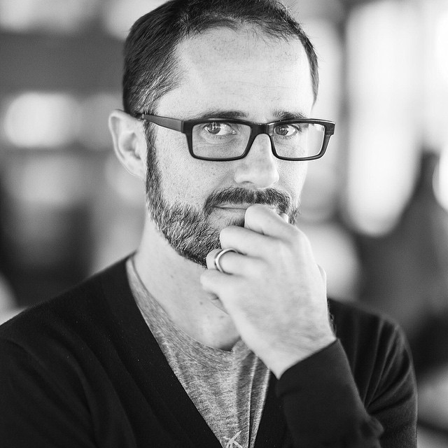 a man wearing glasses with a beard and black cardigan