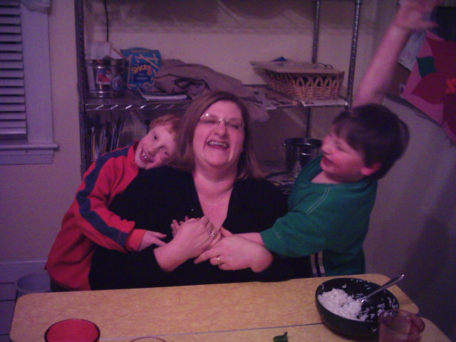 a lady and two boys sitting in front of a table with food